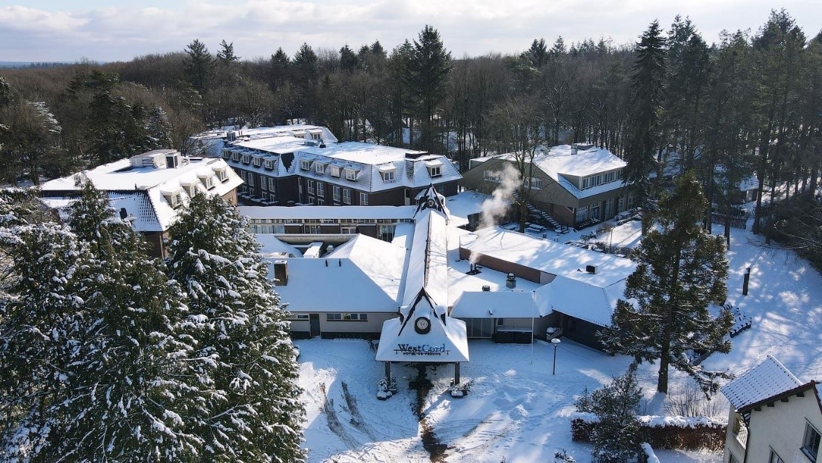 Dronefoto van De Werelt Lunteren in de winter, omringd door besneeuwde bossen op de Veluwe.